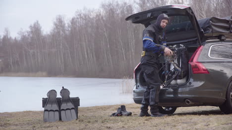 scuba diver in drysuit gets gear ready from car trunk for winter lake ice dive