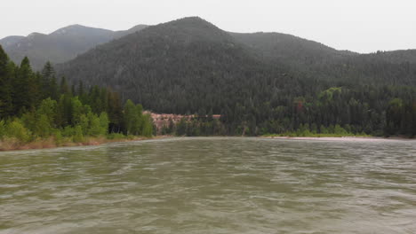 aerial shot of flathead river in montana, camera moves in reverse close to the water, mountains and pine forest in background parallax