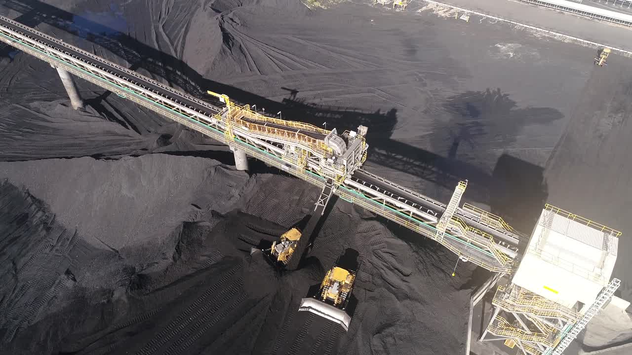 Drone orbiting shot of Coal Mine Plant, Coal coming off conveyor belt with caterpillar mining trucks moving the coal around