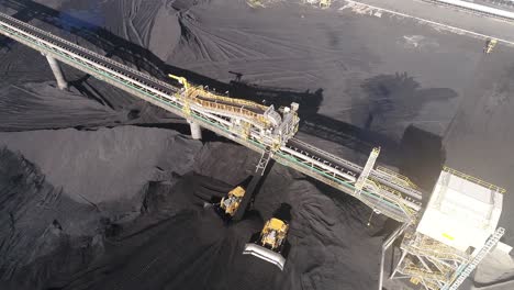 tiro en órbita de drones de la planta de la mina de carbón, carbón que sale de la cinta transportadora con camiones mineros de oruga que mueven el carbón alrededor