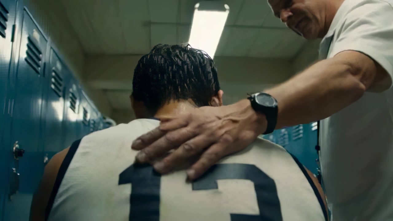 Approaching coach placing pats across back of player in jersey 13 in locker room, offering comfort