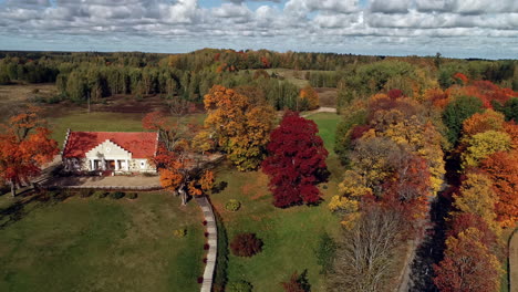 aerial backward moving shot over colorful autumn forest landscape beside beautiful houses by the forest on a cloudy morning