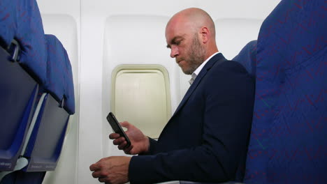 a man with a beard and bald head using cell phone smartphone on an airplane airliner sitting in the passenger cabin