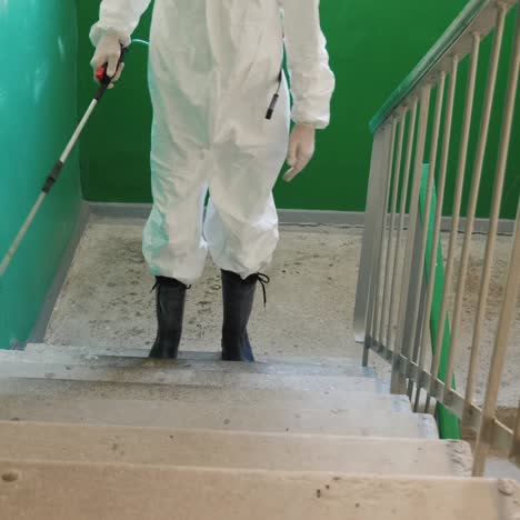 person in protective clothing sprays the stairs of an apartment building with antiseptic