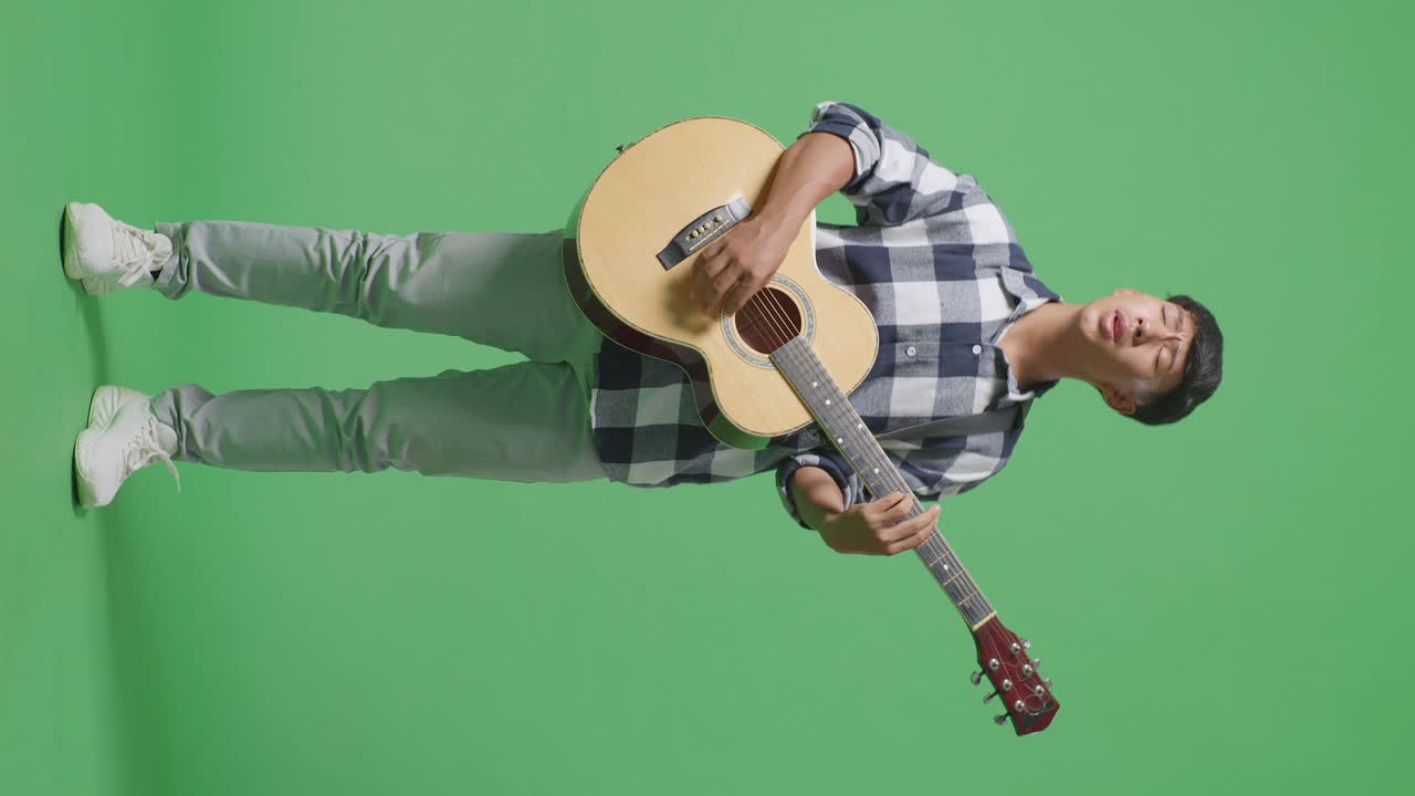 Figura intera di un giovane ragazzo adolescente asiatico che suona la chitarra e canta su sfondo green screen