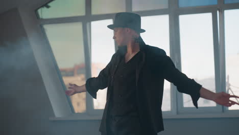white male in black outfit performs fluid dance in smoke filled studio loft with large windows revealing cityscape, stylish choreographed movement conveying modern urban vibe and confident energy