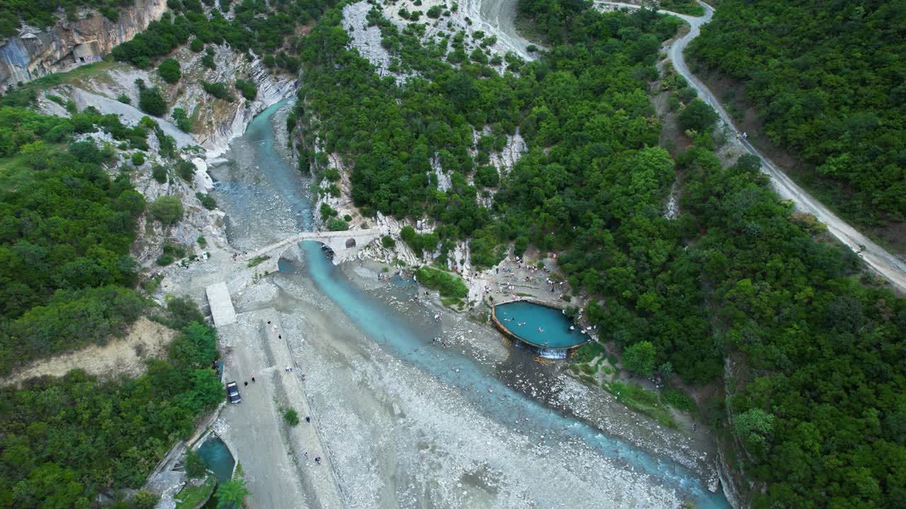 Benje thermal springs river emerald water fills natural pool near ancient stone bridge and tourists