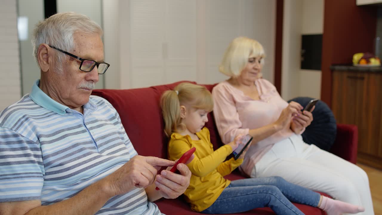 Senior couple grandparents with child girl granddaughter using digital tablet, mobile phone