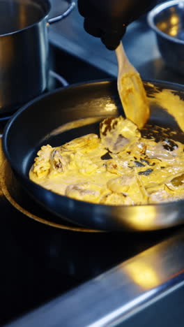 cooking seafood in the pan with white sauce. hand of a cook in latex glove stirs the dish. close up. vertical video.