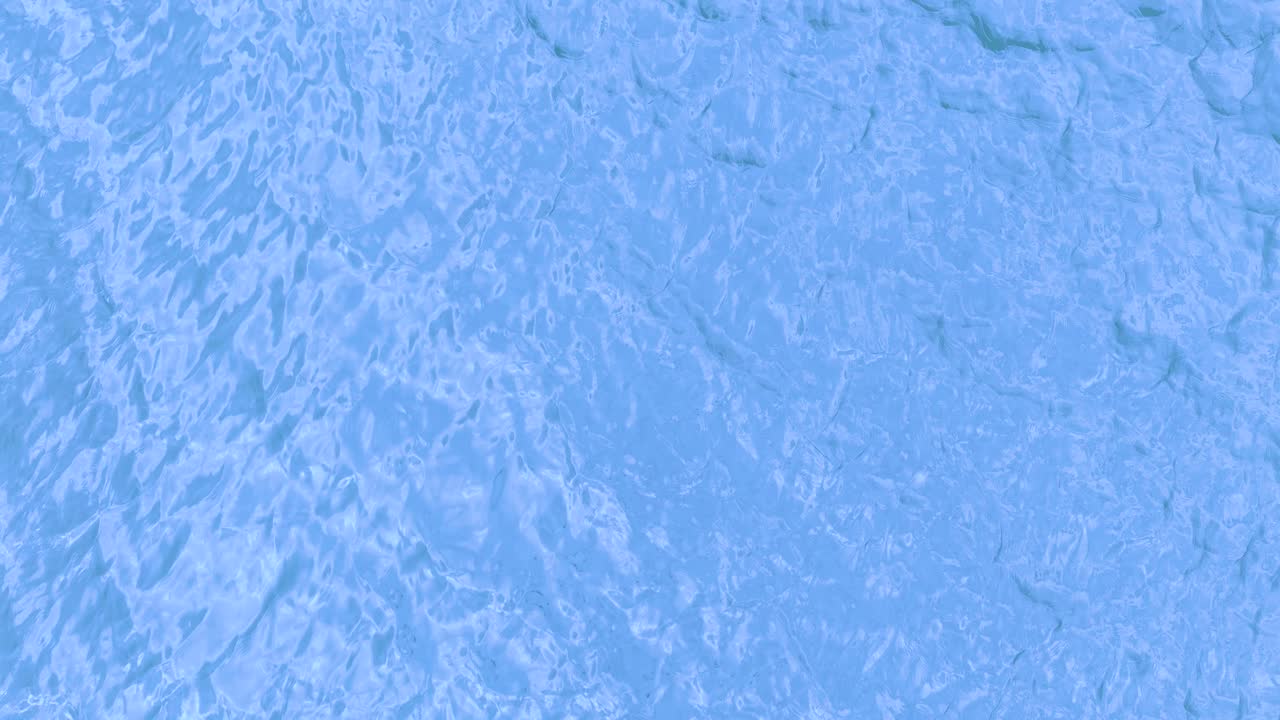 Drone captures tranquil, light blue ocean surface with minimal ripples and soft natural reflections