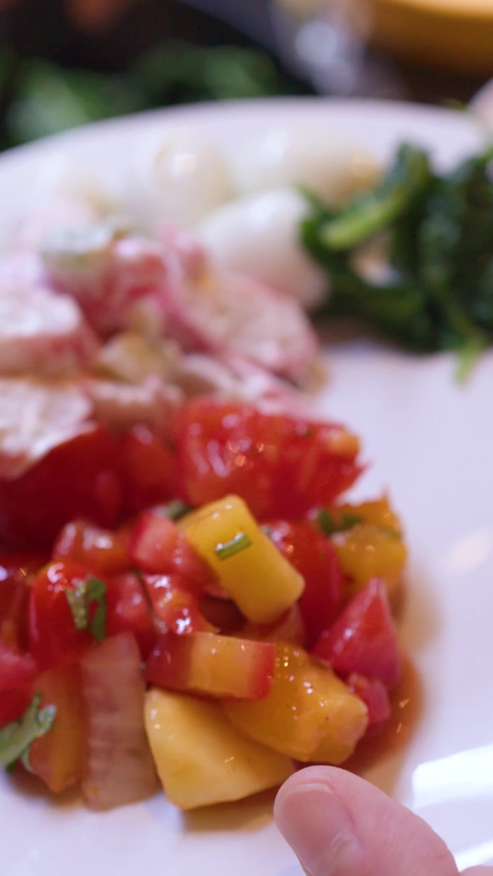 Primo piano di pinze che adagiano verdure verdi su un piatto bianco con vari ingredienti per insalata.
