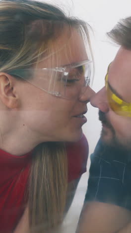 cu: young man and woman in glasses paint glass wall with colors using tools lying on floor smile kissing in room closeup