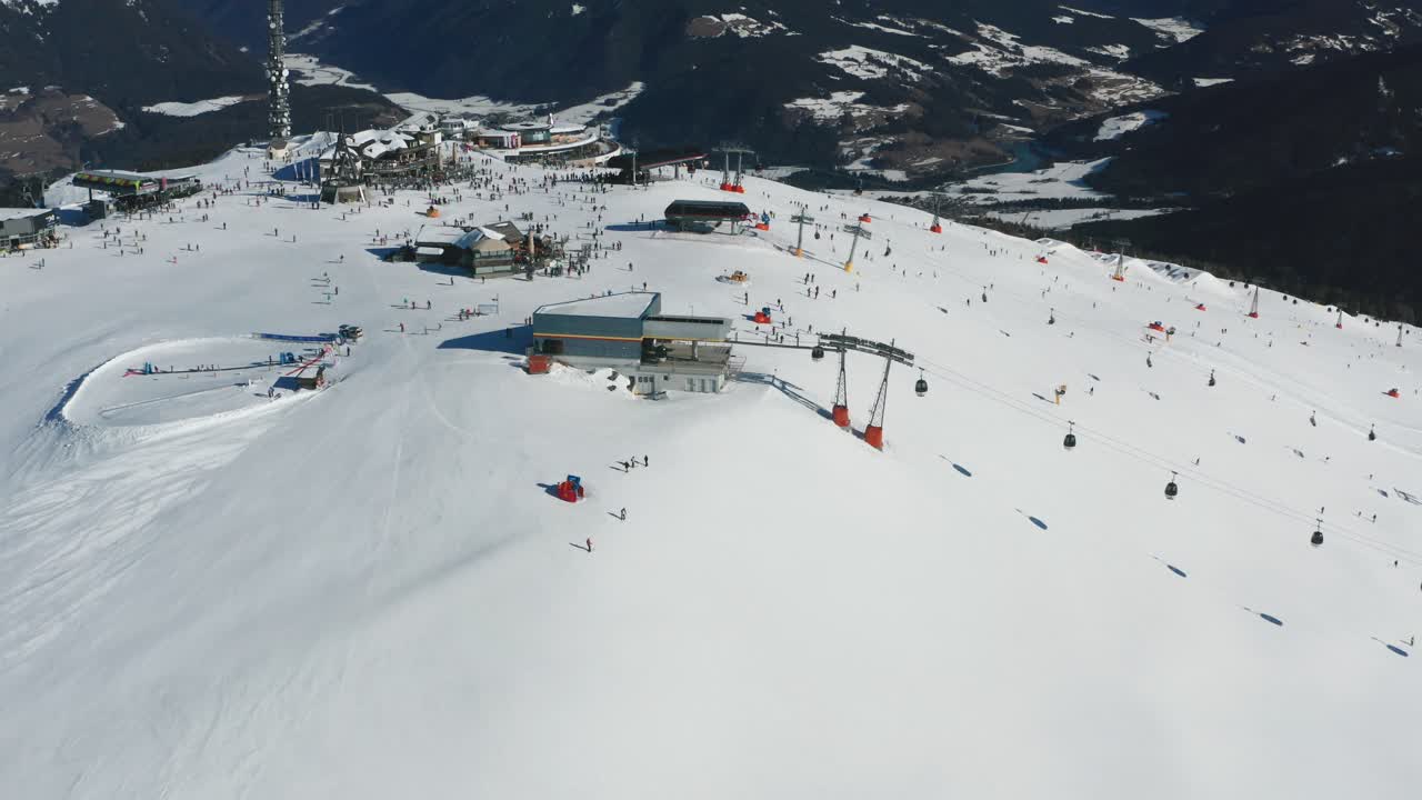Aerial view of the Kronplatz skiing resort in South Tirol, Italy. Cable cars moving, casting shadows on the snow, scores of skiers on the slopes enjoying a lovely, sunny, winter day.