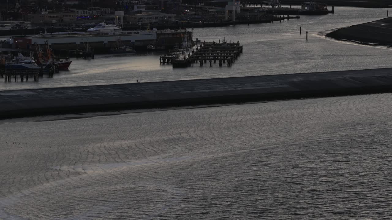Aerial drone video of the industrial sea port of Harlingen, Friesland, at dusk on the Wadden Sea, showcasing a mix of seagoing vessels, ferries, Brown Fleet historic ships, and official service boats