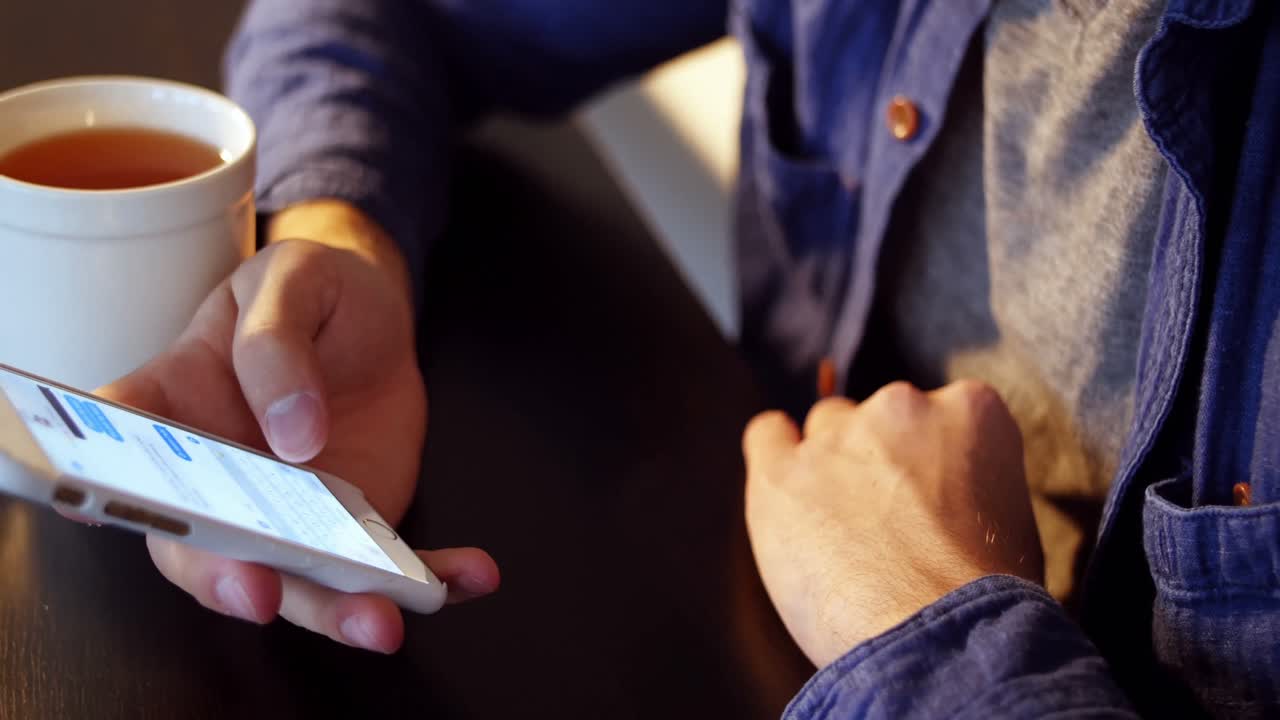 テーブルにブラックコーヒーを置き、スマートフォンを操作する男性の胴体部