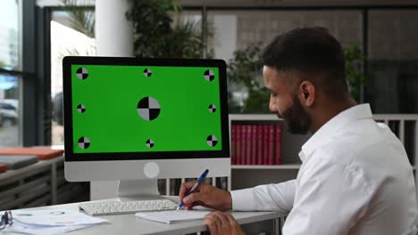 simulacro, pantalla verde, croma. gerente concentrado o dueño de negocio sentado en el escritorio en la oficina, con camisa blanca, escuchando capacitación de negocios en línea, viendo video de entrenador, tomando notas, mejora las habilidades
