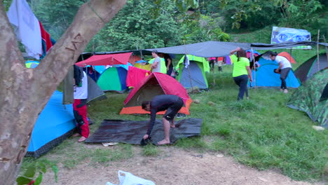 people camping and setting up tents in a lush outdoor environment