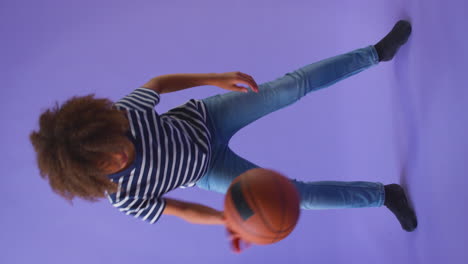 Vertikales-Video-Eines-Jungen,-Der-Mit-Basketball-Vor-Violettem-Hintergrund-Dribbelt