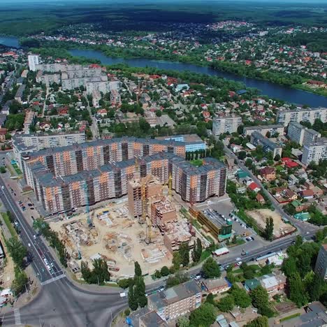 Construction site of a modern district in the city. Urban background with beautiful high-rise buildings, green trees and a blue river. Aerial view.