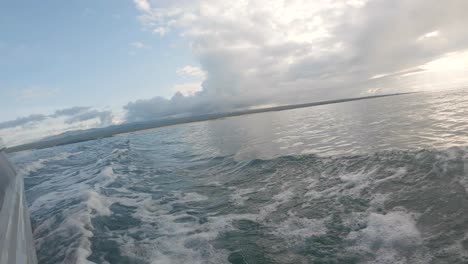 from a boat ride, an island is seen on the back. waves are formed by the motion of the panga. clouds and a blue sky are on the back