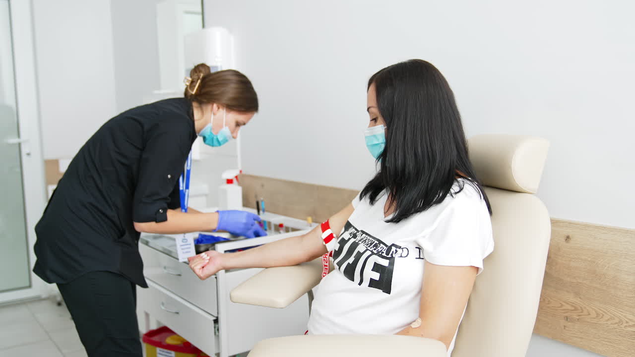 Female nurse taking venous blood from pregnant woman at laboratory. Blood sampling for corona virus antibodies by medical worker indoors. Scientific microbiology test and medical lab equipment.