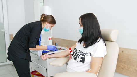 female nurse taking venous blood from pregnant woman at laboratory. blood sampling for corona virus antibodies by medical worker indoors. scientific microbiology test and medical lab equipment.