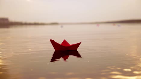 red paper boat floating alone with the slow motion in the river at sunset. lovely kid's origami ship on water surface in the evening. close-up