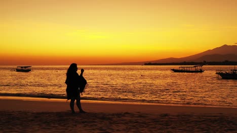 mujer de pie en la arena de una playa viendo el brillo dorado de la puesta de sol de la tarde