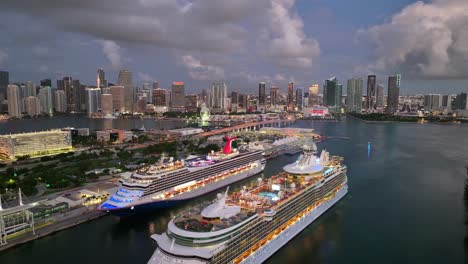 cruise ships docked at port of miami with downtown miami skyline glowing at dusk. the waterway, large vessels, and city skyline create a vibrant harbor scene. aerial.