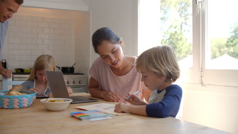 Niños-Trabajando-En-La-Mesa-De-La-Cocina-Con-Mamá,-Mientras-Papá-Cocina.