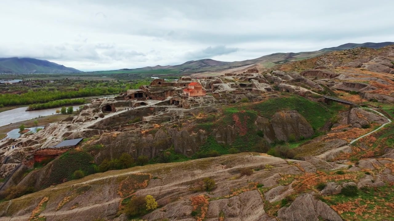 Vista aerea con drone della città rupestre di Uplistsikhe in Georgia che mostra antiche strutture scavate nella roccia, scogliere drammatiche e paesaggi circostanti della valle fluviale.