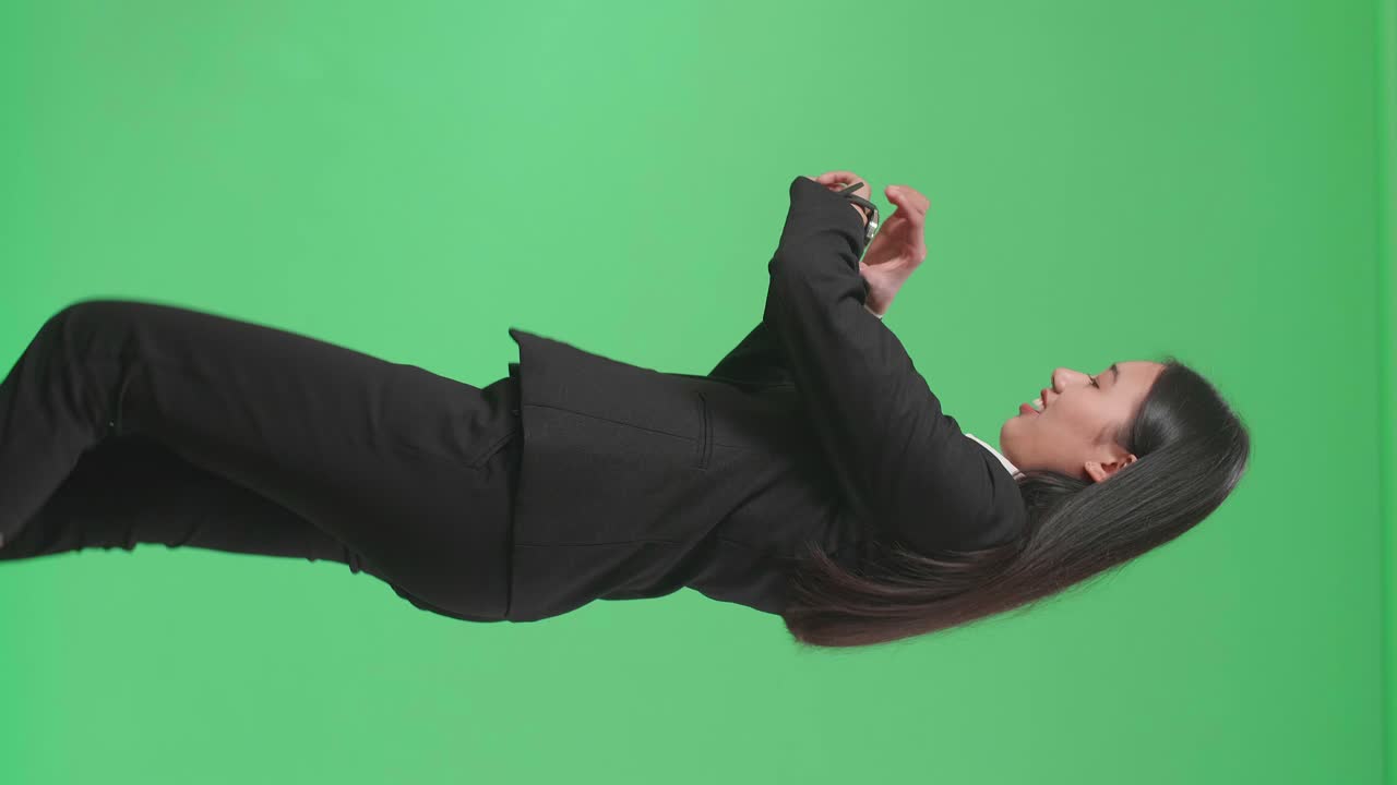 Side View Of A Smiling Asian Business Woman Looking At A Watch While Walking Through Green Screen In The Studio