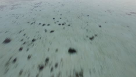 Komodo-Island-Indonesia---fast-speed-flying-at-low-altitude-over-shallow-ocean-water-and-tilting-up-towards-silhouetted-islands-on-the-horizon