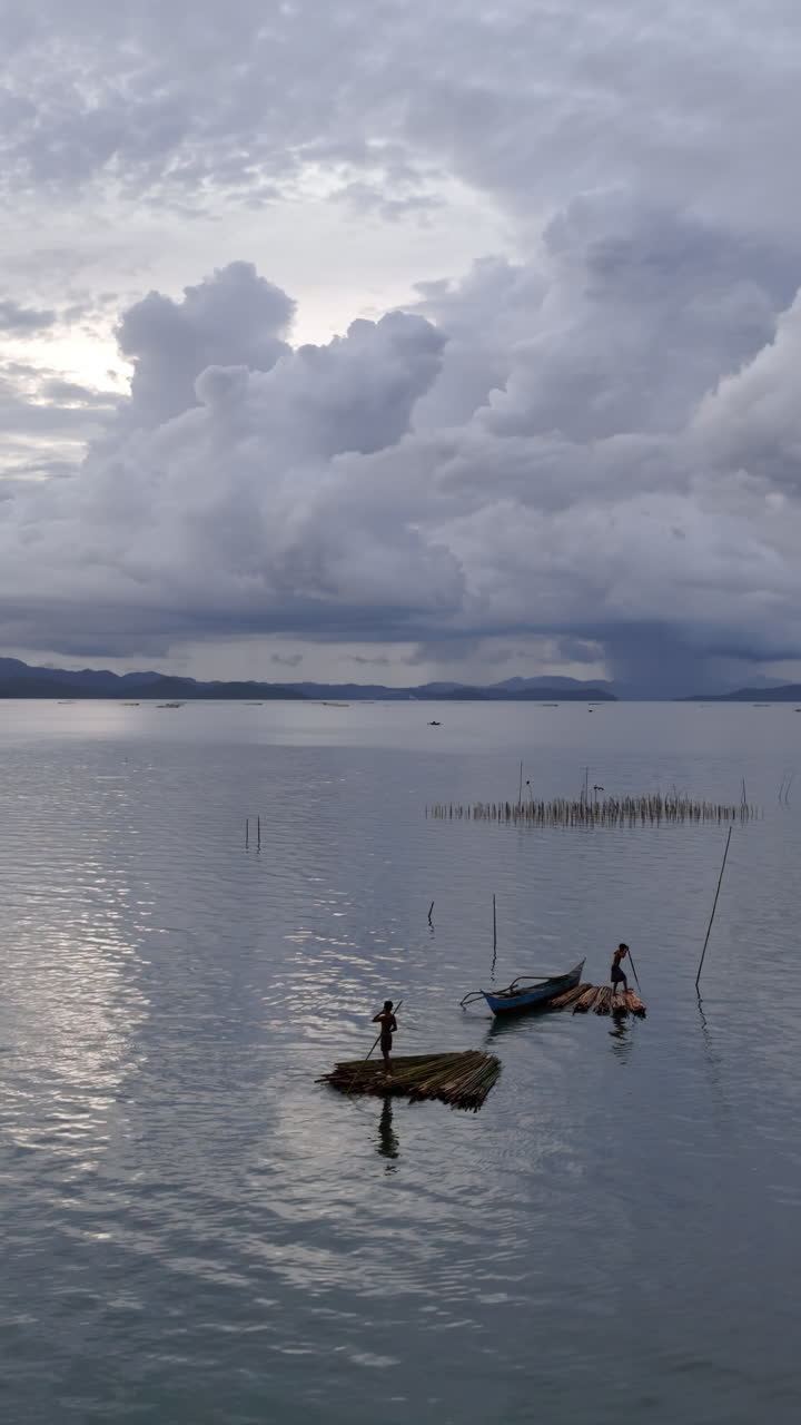 Vista aérea con dron de pescadores en pequeñas embarcaciones al atardecer sobre aguas en calma con montañas al fondo en Filipinas. Vertical