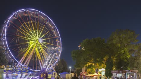 rotating in motion illuminated attraction ferris wheel and brightly carousel merry-go-round on summer evening in city amusement park.