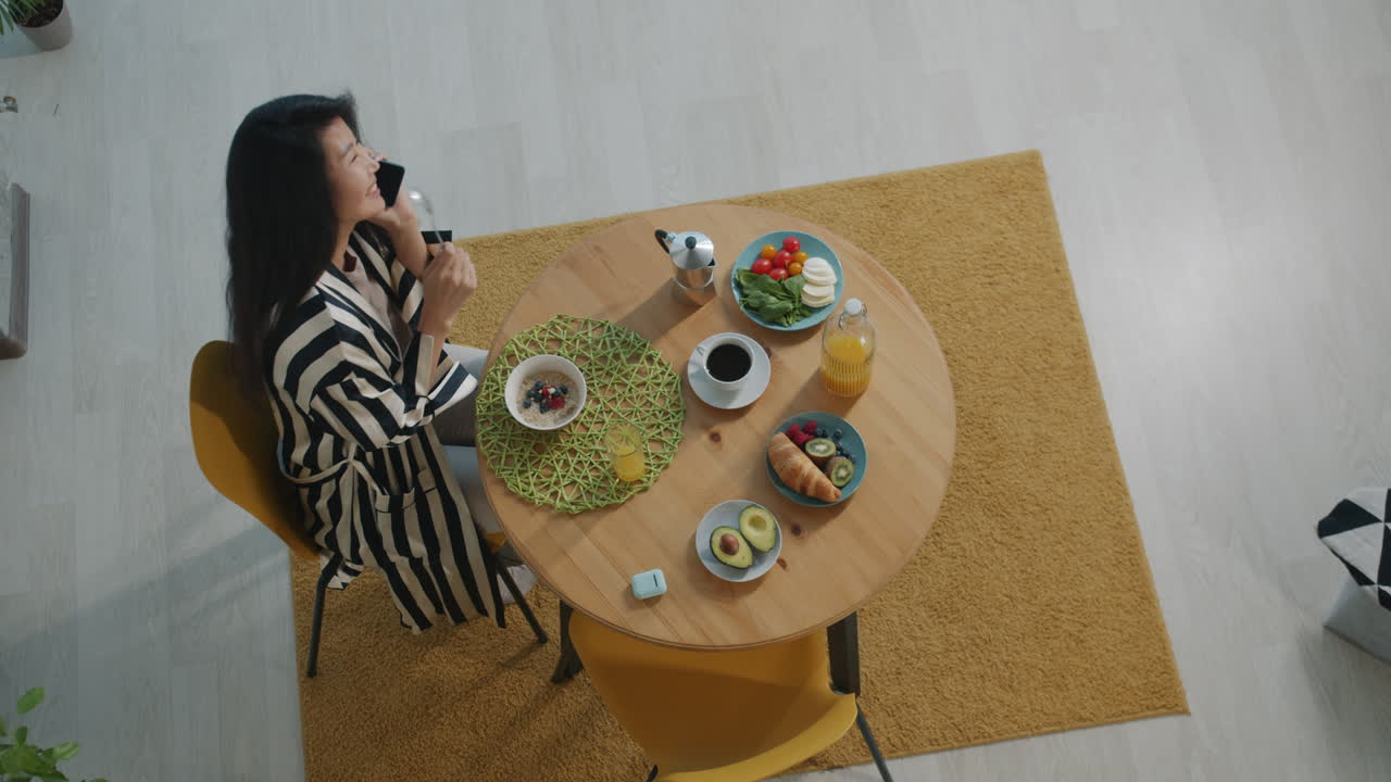 Woman Eating Breakfast and Talking on Phone