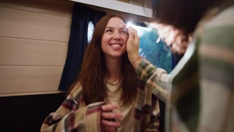 Over-the-shoulder-of-a-brunette-guy-in-a-checkered-shirt-stroking-his-brunette-girlfriend-on-the-cheek-and-talking-to-her-during-his-vacation-in-a-trailer-in-a-camp-during-a-picnic-in-the-summer-outside-the-city