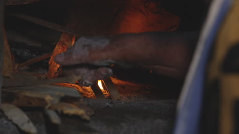 a woman putting small pieces of woods in a rustic old oven