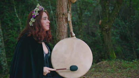 druid girl in a forest playing a shamanic drum side view wide shot