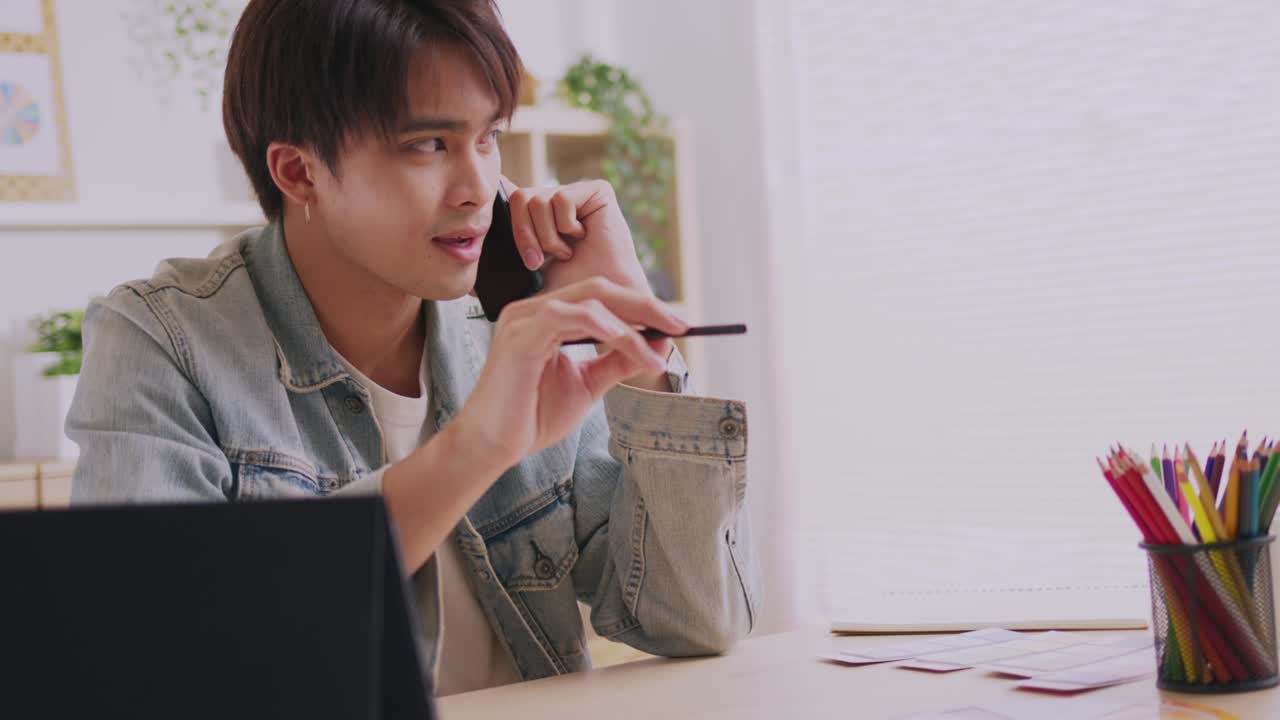 아시아인 디자이너는 스마트폰으로 커뮤니케이션을 하고, 프로젝트와 서류 작업을 하며, 노트북으로 책상에서 집에서 일합니다.