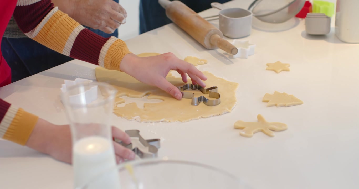 Adult and child hands reaching, pressing cutters into dough on counter, cutting cookies for baking