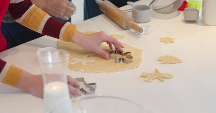 Adult and child hands reaching, pressing cutters into dough on counter, cutting cookies for baking
