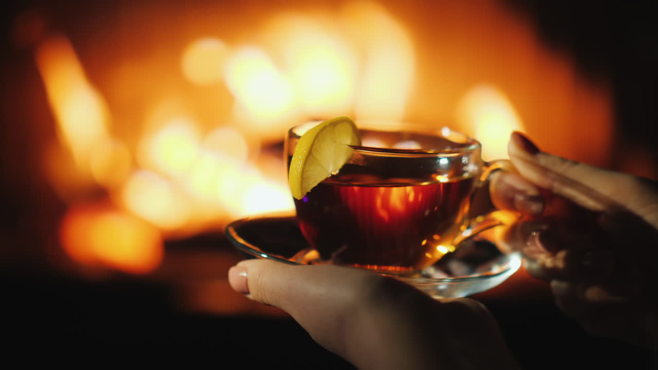 벽난로 옆에 놓인 컵을 들고 있는 여성의 손은 겨울 개념에서 따뜻하게 유지됩니다