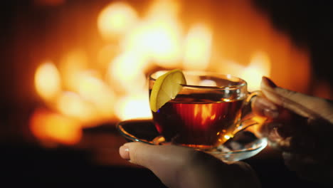 frauenhände mit einer tasse am kamin halten im winterkonzept warm