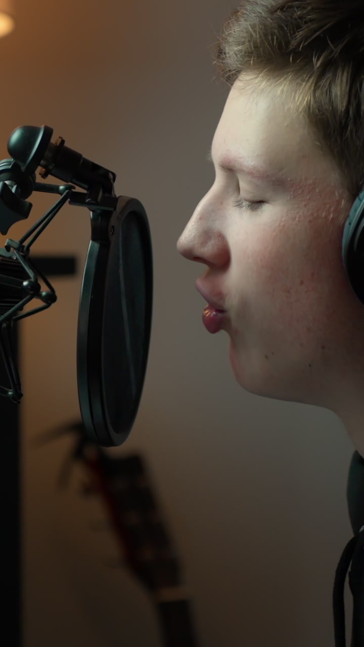 A teenage singer wearing headphones while recording his vocals in the studio, closeup vertical shot