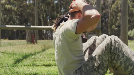 grupo diverso de soldados haciendo abdominales en el campo, en el curso de obstáculos del ejército en el sol