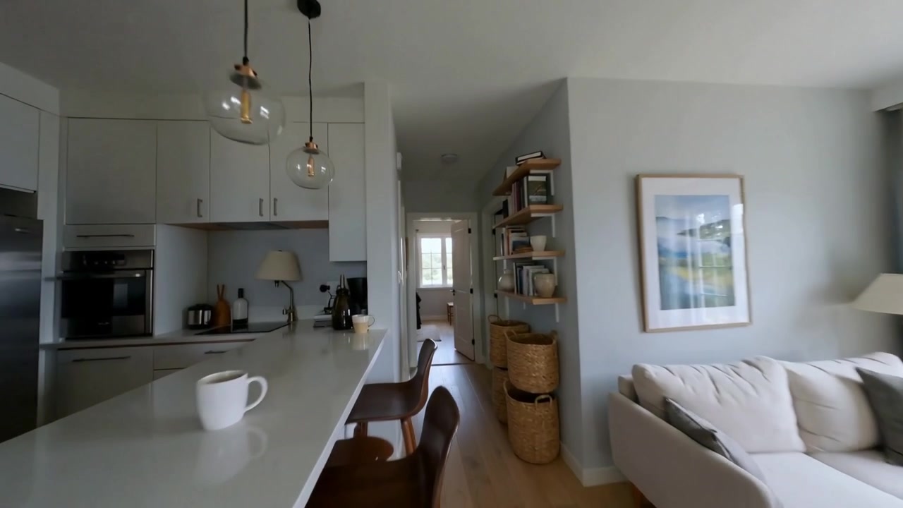 Entrando por la puerta, la cámara revela una cocina y sala de estar de concepto abierto, mostrando una taza blanca y estantes.