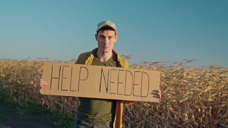 man holding sign asking for help in cornfield