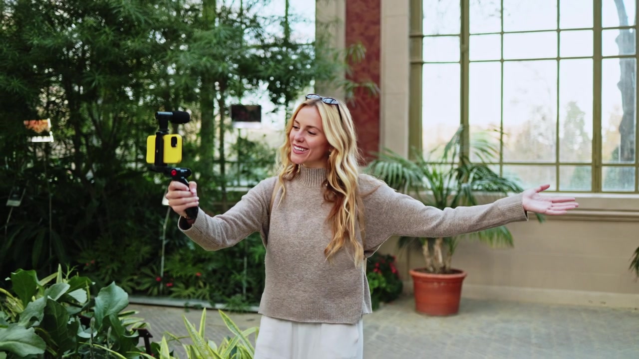 Donna allegra che fa vlogging con smartphone e microfono in serra