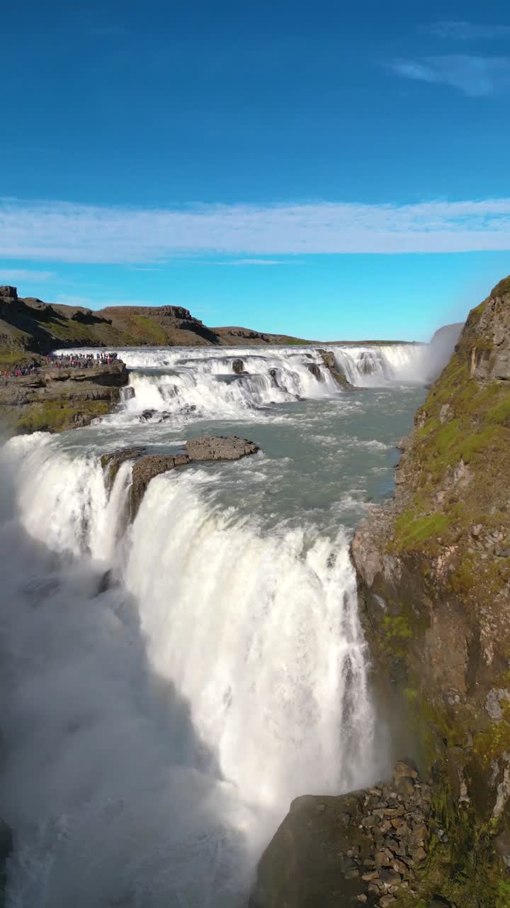 4K Aerial view of Gullfoss Falls, one of Iceland’s most iconic natural landmarks, showing mist rising from the gorge and sunlight creating glistening rainbows above the spray. Iceland_06